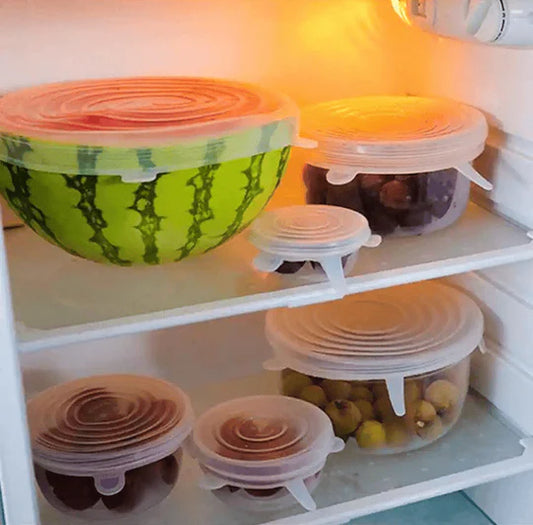 Stackable silicone food storage containers with lids on a refrigerator shelf.